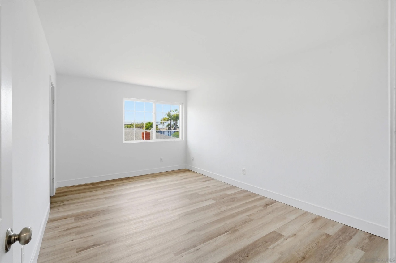 An empty bedroom with new plank flooring and a window framing a tall palm and a glimpse of the bay