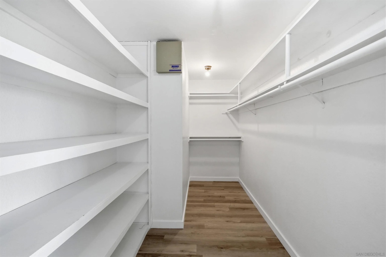 A long walk-in closet lined with white shelving on the left and hanging rods on the right, new plank flooring underfoot
